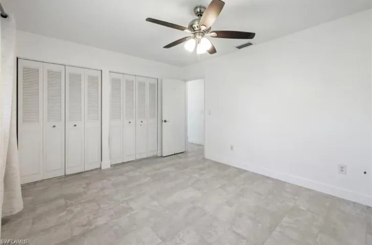 Spacious room featuring light-toned tile flooring, white walls, and a ceiling fan with integrated lighting