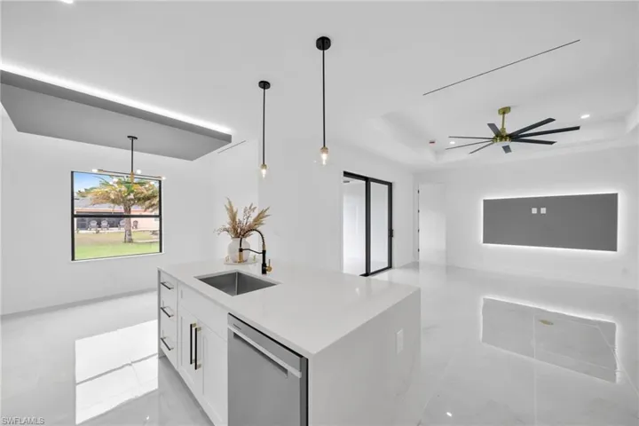 Kitchen with a sink, white cabinetry, stainless steel dishwasher, a raised ceiling, and pendant lighting