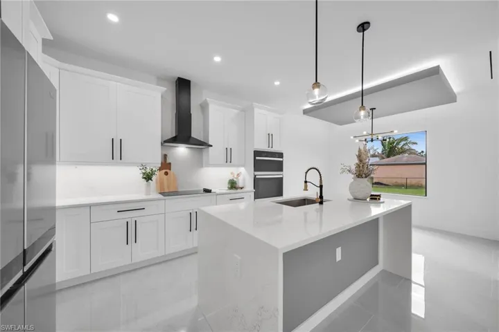 Kitchen with black appliances, wall chimney range hood, white cabinets, and a sink