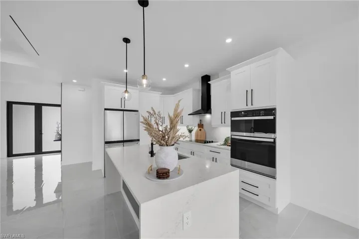 Kitchen with wall chimney range hood, a kitchen island with sink, appliances with stainless steel finishes, and white cabinets
