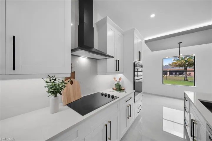 Kitchen featuring white cabinets, wall chimney exhaust hood, hanging light fixtures, light stone countertops, and black electric cooktop
