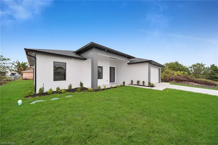View of front facade with a garage, concrete driveway, a front lawn, and stucco siding
