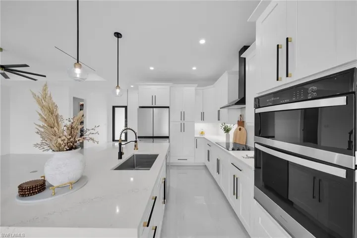 Kitchen featuring double oven, white cabinets, freestanding refrigerator, wall chimney exhaust hood, and decorative light fixtures