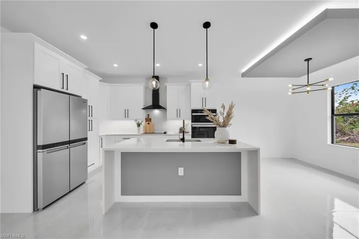 Kitchen featuring wall chimney range hood, white cabinetry, light countertops, and freestanding refrigerator