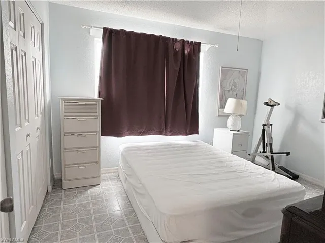 Bedroom with a textured ceiling, a closet, baseboards, and light tile patterned floors