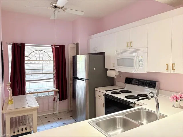 Kitchen with white microwave, electric range oven, a sink, white cabinetry, and light countertops