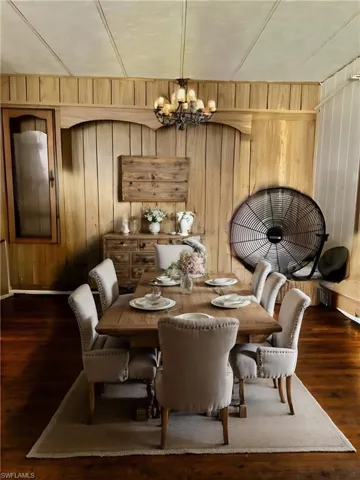 Virtually Staged: Dining space featuring wood walls, dark wood-type flooring, and a notable chandelier