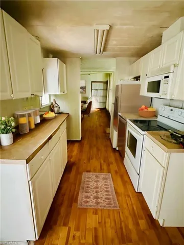 Virtually Staged: Kitchen featuring hardwood / wood-style flooring, white appliances, and white cabinets