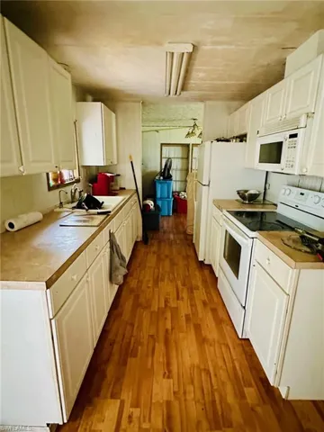 Kitchen with sink, white appliances, hardwood / wood-style floors, and white cabinets