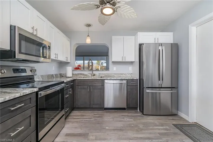 Kitchen featuring sink, stainless steel appliances, white cabinets, and light stone countertops
