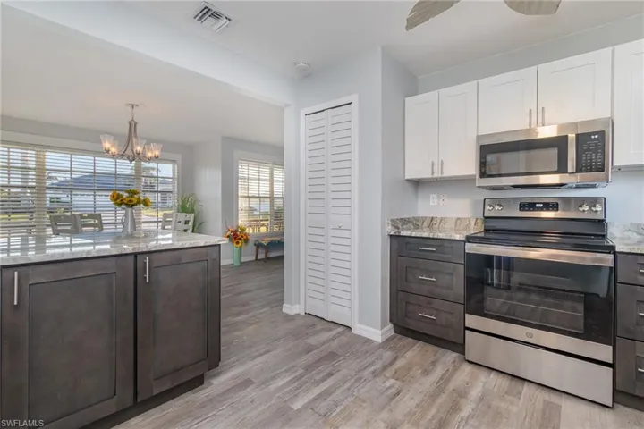 Kitchen with white cabinetry, light stone counters, a chandelier, light wood-type flooring, and appliances with stainless steel finishes