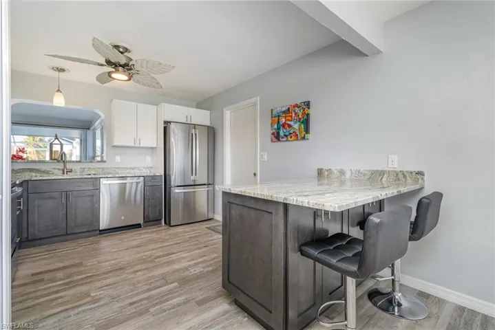 Kitchen with sink, appliances with stainless steel finishes, pendant lighting, light stone countertops, and white cabinets