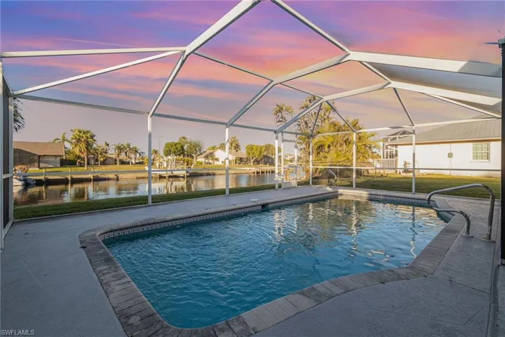 Pool at dusk with a water view, a patio, and a lanai