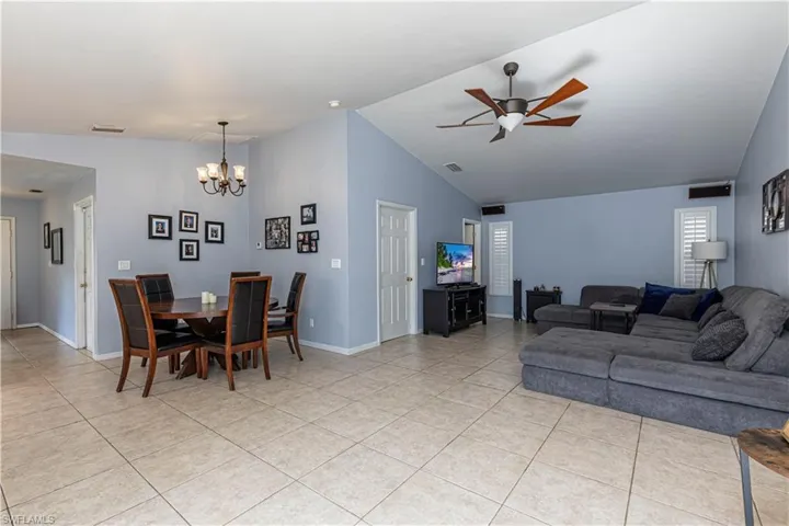 Living room with a ceiling fan, vaulted ceiling, light tile patterned floors, and a chandelier