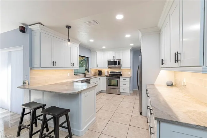 Kitchen featuring a peninsula, decorative backsplash, appliances with stainless steel finishes, light stone counters, and recessed lighting
