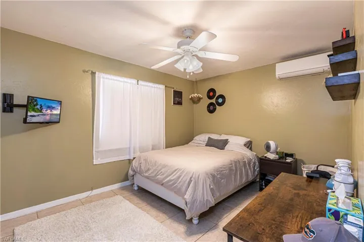 Bedroom with a wall mounted air conditioner, a ceiling fan, and light tile patterned flooring