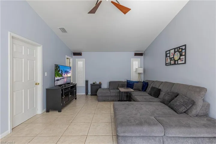 Living room with vaulted ceiling, light tile patterned floors, and a ceiling fan