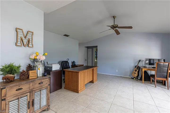 Home office featuring lofted ceiling, light tile patterned flooring, and a ceiling fan