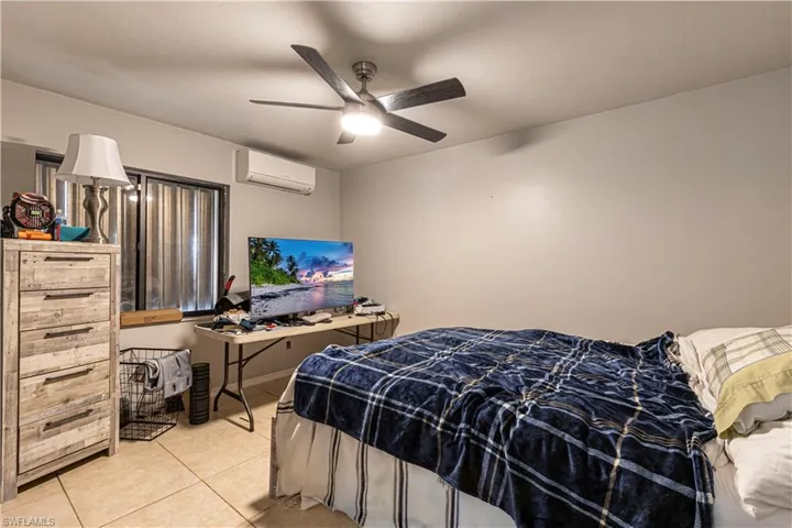Bedroom featuring light tile patterned floors, a wall unit AC, and ceiling fan