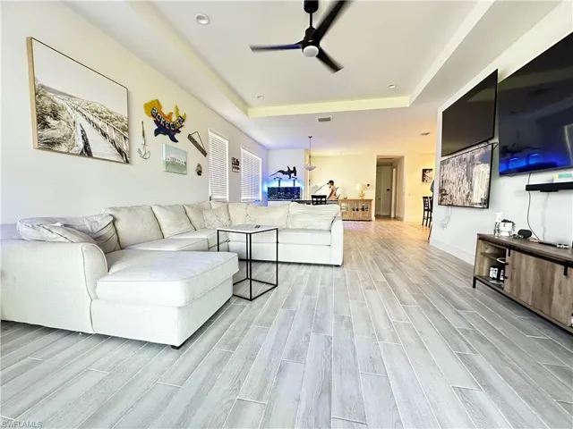 Living space featuring wood-finish flooring, tray ceiling, and a modern ceiling fan with integrated lighting