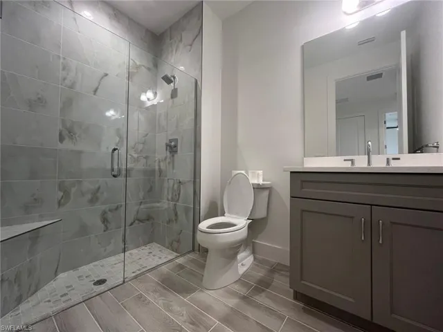 Bathroom featuring a walk-in shower with large-format stone-finish tile surround, built-in bench seating, frameless glass enclosure, dark-toned shaker-style vanity with stone-finish countertop, and wood-finish tile flooring