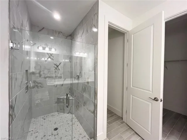 Walk-in shower featuring large-format stone-look tile walls, a built-in corner seat, a glass enclosure, and a mosaic tile floor, paired with a two-panel interior door