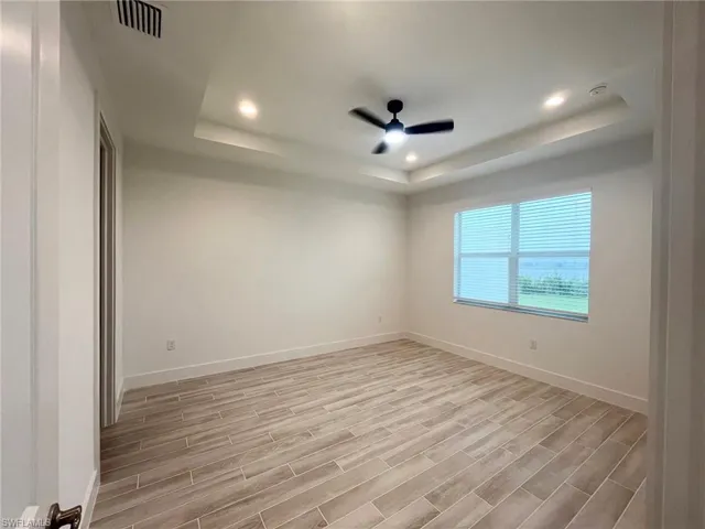 Tray ceiling featuring recessed lighting and a central ceiling fan, paired with wood-finish tile flooring and a multi-pane window