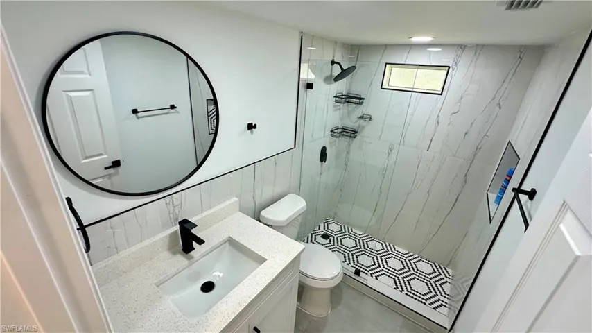 Bathroom with decorative backsplash, tile walls, a marble finish shower, toilet, and vanity