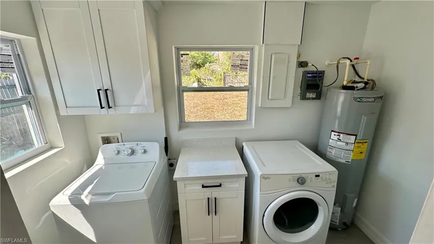 Laundry area featuring washing machine and clothes dryer, electric panel, baseboards, cabinet space, and electric water heater