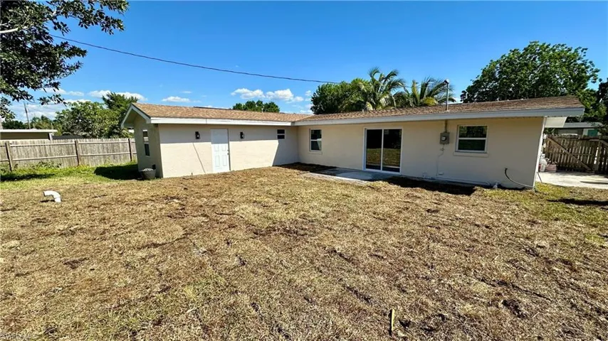 Rear view of house featuring stucco siding, fence, and a lawn