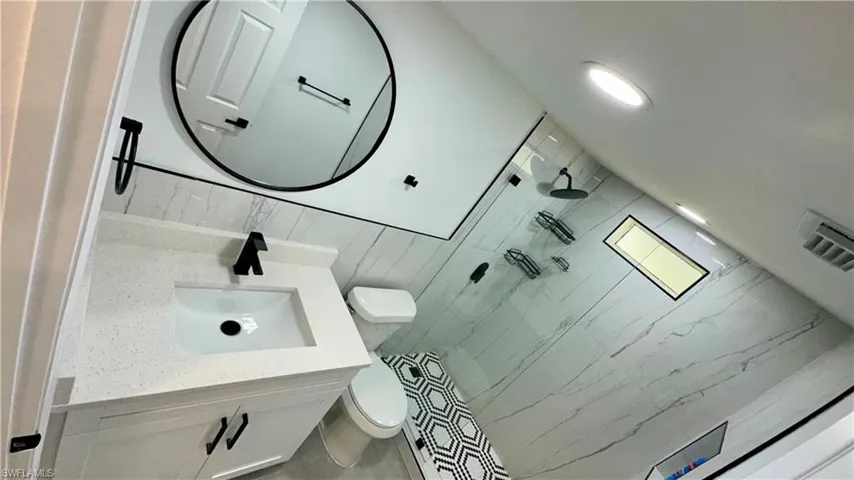 Bathroom featuring visible vents, walk in shower, toilet, vanity, and backsplash