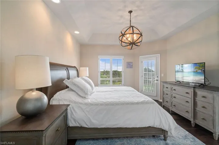 Primary bedroom with custom lighting, en-suite primary bathroom and wood flooring with balcony access.