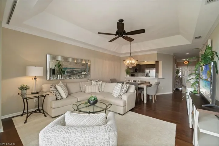 Great room with a vaulted ceiling, wood floors, custom lighting and crown molding facing the dining area and kitchen.