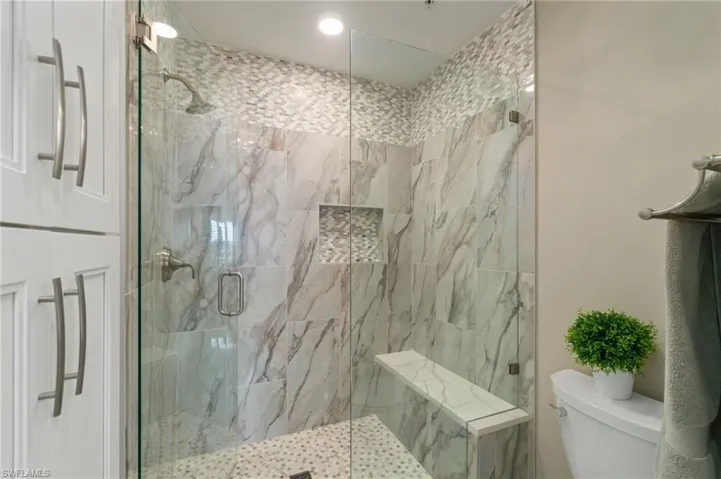 Renovated guest bathroom featuring white cabinetry, toilet and a tile walk-in shower.