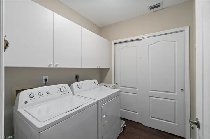 Laundry room featuring white cabinetry, finished floors, washer and dryera and storage area.
