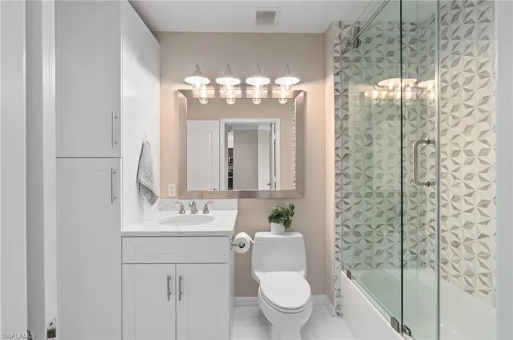 Renovated guest bathroom featuring white cabinetry, toilet and a tile walk-in shower.