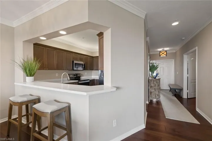 Kitchen with wood cabinetry, stainless steel appliances,wood flooring, a breakfast bar area, and recessed lighting.