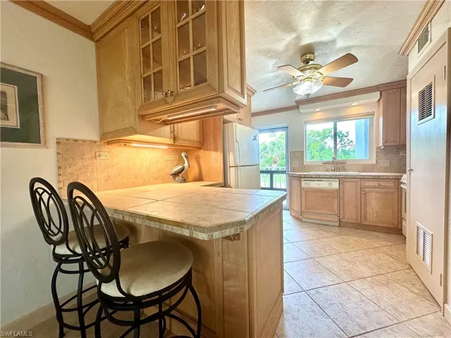 Kitchen featuring a breakfast bar, freestanding refrigerator, dishwasher,  backsplash, and a ceiling fan