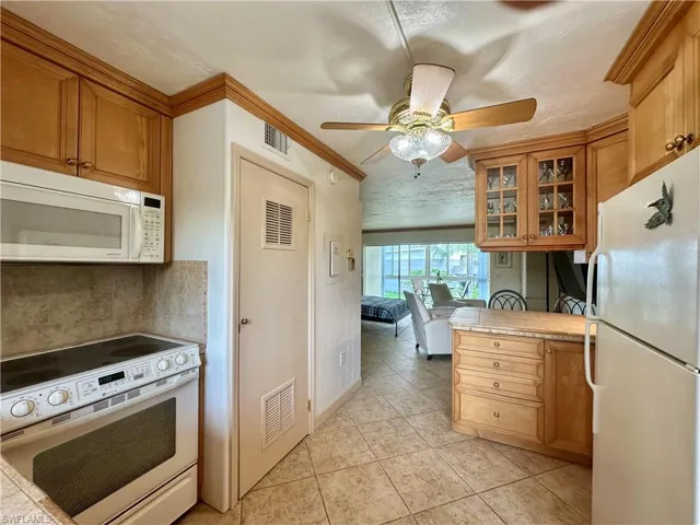 Kitchen with white appliances, tan cabinetry, glass insert cabinets, and tile countertops. New water heater