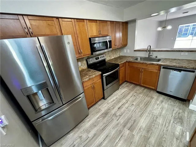 Kitchen featuring pendant lighting, sink, backsplash, appliances with stainless steel finishes, and light hardwood / wood-style floors