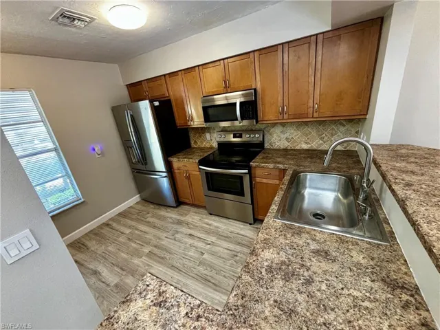 Kitchen featuring light hardwood / wood-style floors, a textured ceiling, sink, stainless steel appliances, and backsplash