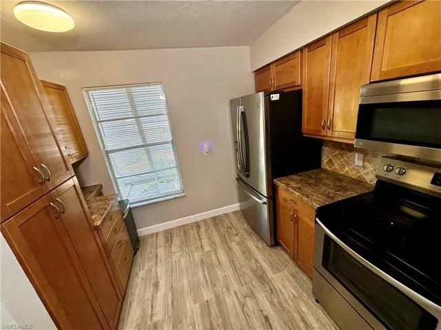 Kitchen featuring light hardwood / wood-style floors, vaulted ceiling, decorative backsplash, appliances with stainless steel finishes, and dark stone countertops