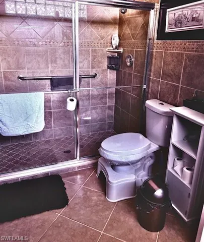Bathroom with tile patterned floors, toilet, a shower with door, and tile walls