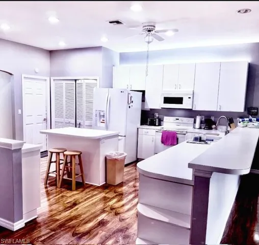 Kitchen with a breakfast bar, white appliances, dark wood-type flooring, white cabinets, and a kitchen island