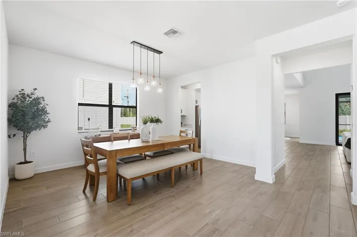 Dining space featuring light wood-finish flooring, a contemporary linear chandelier with five exposed bulbs, a large window with horizontal blinds, and clean white walls
