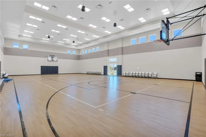 Spacious indoor court featuring wood-finish flooring with court markings, multiple overhead lighting fixtures, and high-set windows