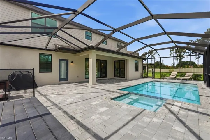 Screened outdoor living area featuring an in-ground swimming pool with an integrated spa, expansive paver patio, multi-level home exterior, and transom windows