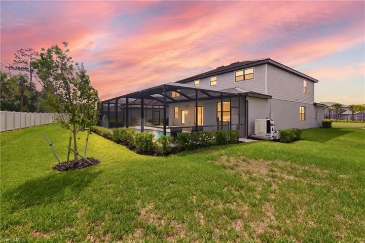 Rear exterior featuring a screened-in swimming pool, a concrete patio, and a manicured lawn