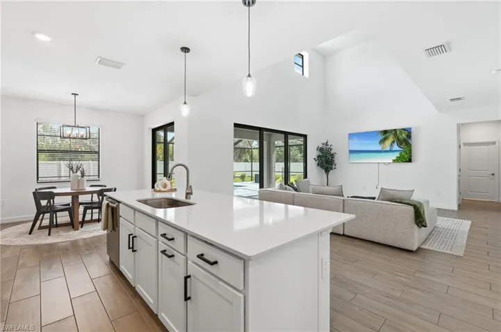Open-concept kitchen and living area featuring a large center island with a stainless steel sink and white cabinetry