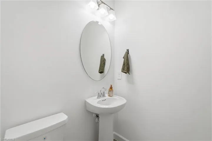 First Pedestal sink with a chrome faucet, illuminated by a three-light vanity fixture